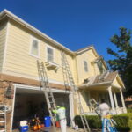 Professional exterior painter working from a ladder on a beige two-story home