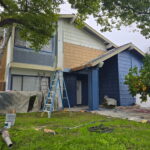 Exterior painter working from a ladder on blue and gray siding