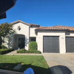 Completed cream stucco home exterior with dark garage doors