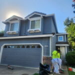 House painter applying exterior paint to a gray two-story home