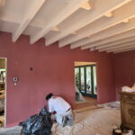 Painter applying red wall paint beneath white patio beams