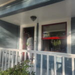 Painter working on red accent trim around a covered porch window