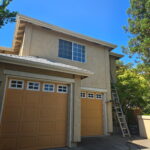 Exterior house painter working from a ladder beside tan garage doors