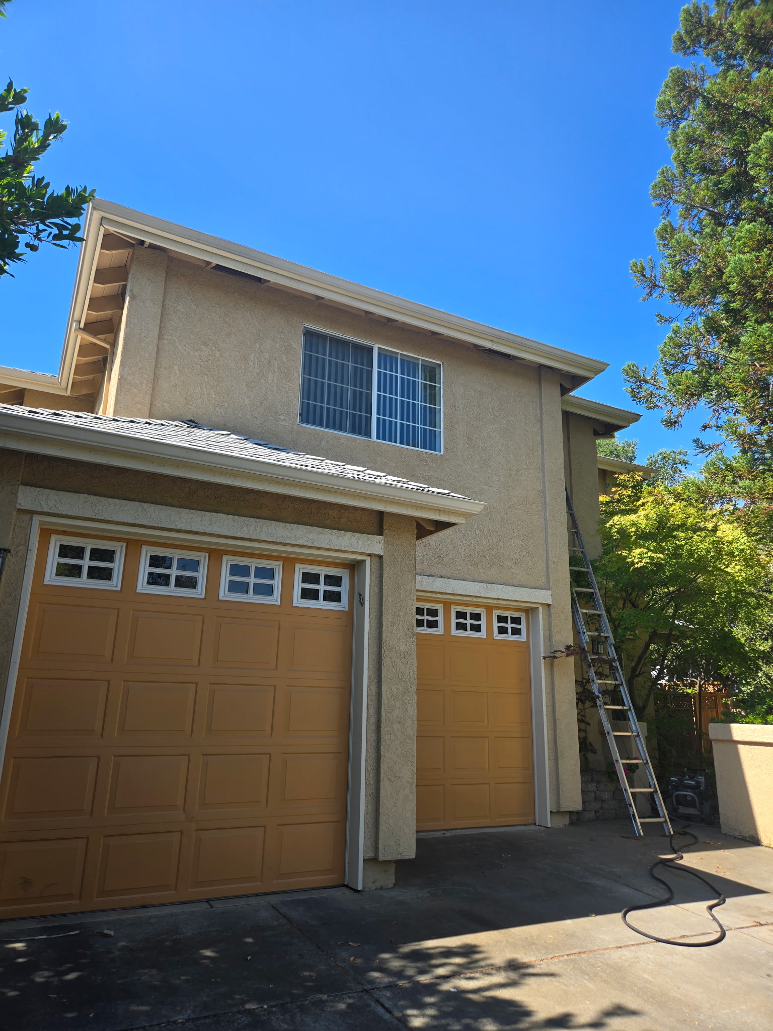 Exterior house painter working from a ladder beside tan garage doors