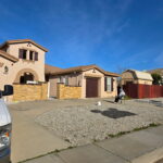 Completed tan stucco house painting project with dark brown garage doors