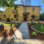 Renovated yellow stucco home exterior with dark trim and landscaped walkway